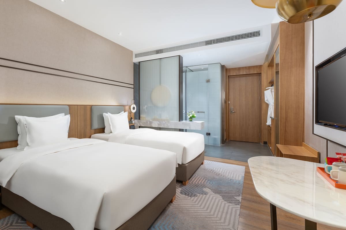 A modern hotel room with two beds, a large mirror, a TV, and a small table with a tray.