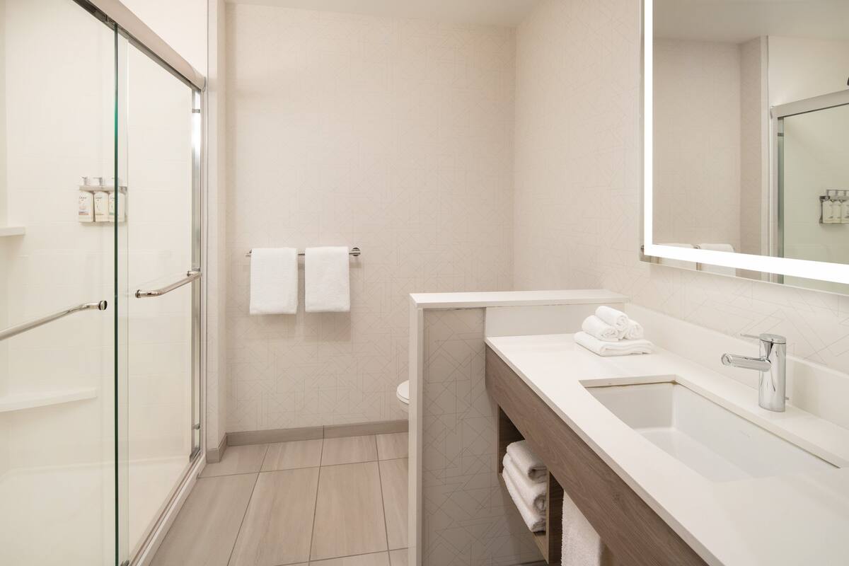 A modern bathroom with a glass shower enclosure, a white sink with a mirror, and a toilet with two white towels hanging on the wall.