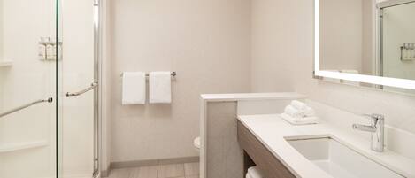 A modern bathroom with a glass shower enclosure, a white sink with a mirror, and a toilet with two white towels hanging on the wall.