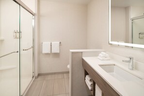 Un baño moderno con cabina de ducha de vidrio, un lavamanos blanco con espejo y un inodoro con dos toallas blancas colgadas en la pared.