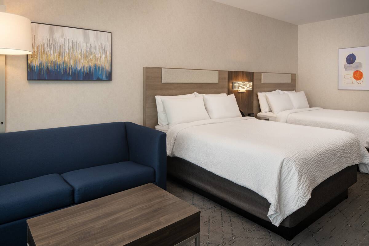 A hotel room with two beds, a blue sofa, a wooden table, and artwork on the walls.