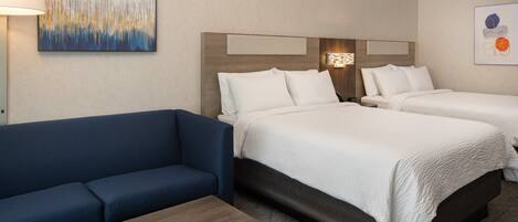 Habitación de hotel con dos camas, un sofá azul, una mesa de madera y obras de arte en las paredes.