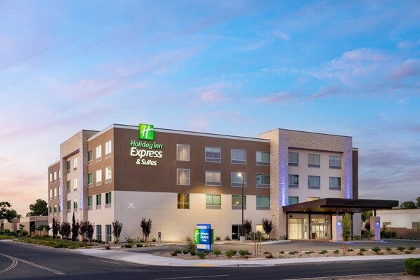 Un hotel Holiday Inn Express & Suites con diseño moderno, que presenta un letrero llamativo, un acceso cubierto y un jardín delantero ajardinado.