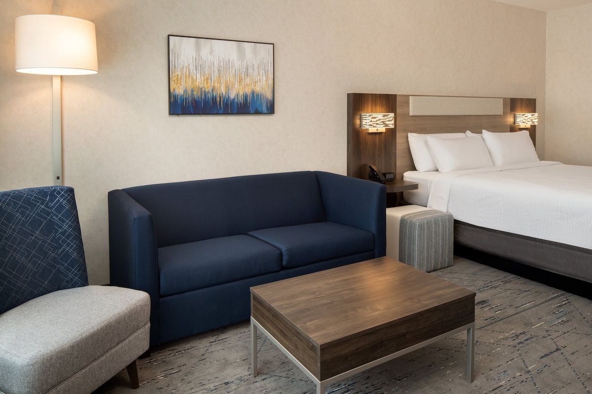 Une chambre d’hôtel avec un lit, un canapé bleu, un petit fauteuil, une table basse en bois et une lampe sur pied.