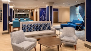 A modern hotel lobby with a sofa, two armchairs, a coffee table, and a seating area with a blue wall mural. - Holiday Inn Express & Suites Fresno Airport by IHG (Fresno)