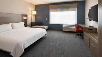 Quarto de hotel com uma cama grande, uma escrivaninha com cadeira, televisão e janela com vista.