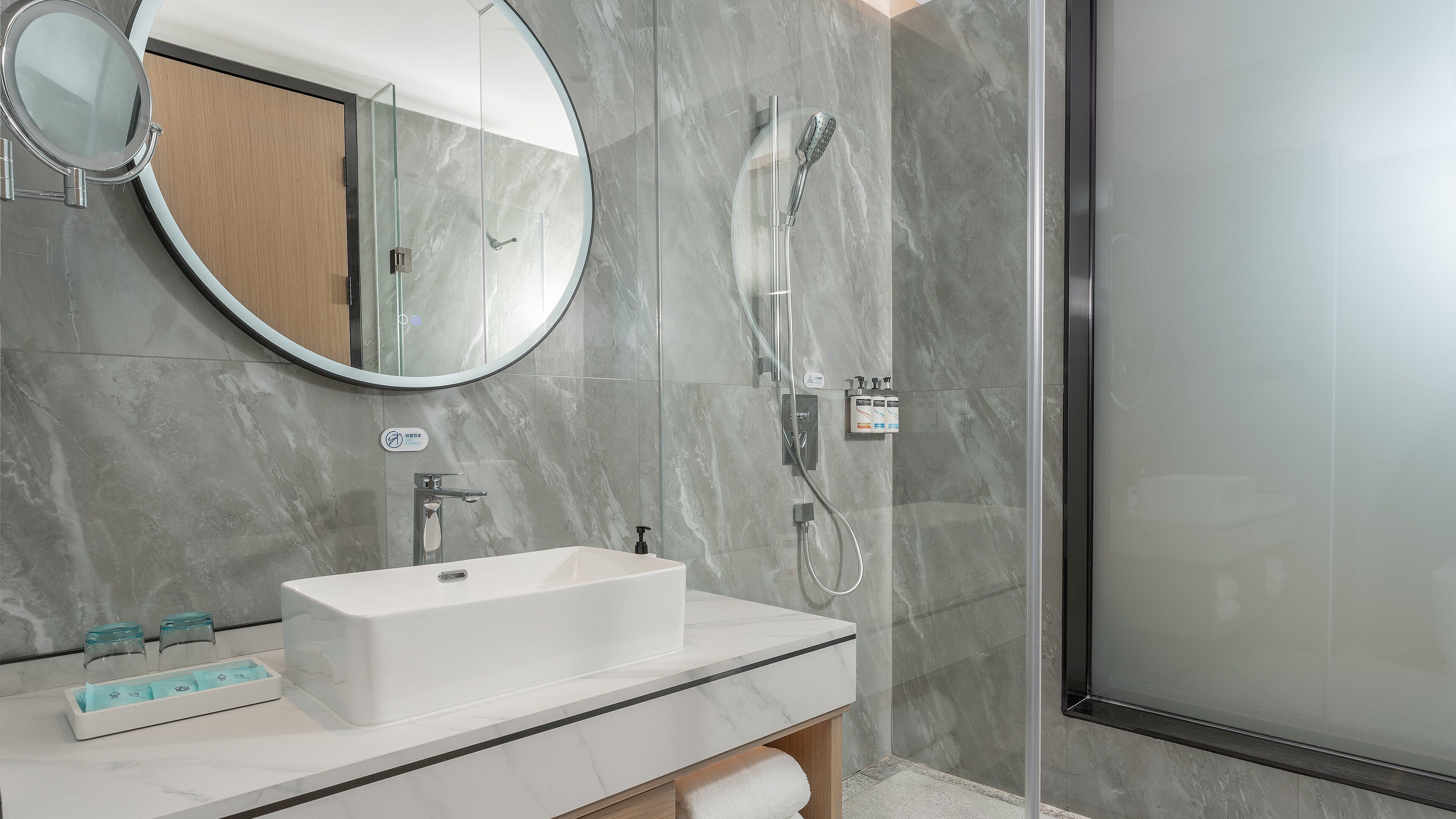 Une salle de bain moderne avec un lavabo rectangulaire, un miroir rond et une douche à parois de verre.