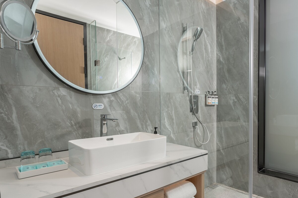 A modern bathroom with a rectangular sink, a round mirror, and a glass-enclosed shower.