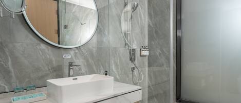 Un baño moderno con un lavamanos rectangular, un espejo redondo y una ducha con mampara de vidrio.