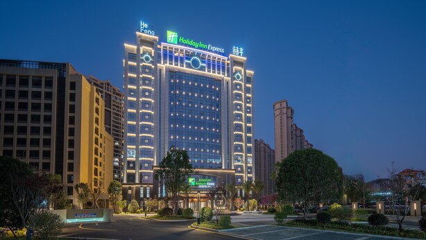 A multi-story Holiday Inn Express building with illuminated signage, surrounded by other high-rise buildings and well-maintained landscaping. - Holiday Inn Express Quanzhou Taishang by IHG (Quanzhou)