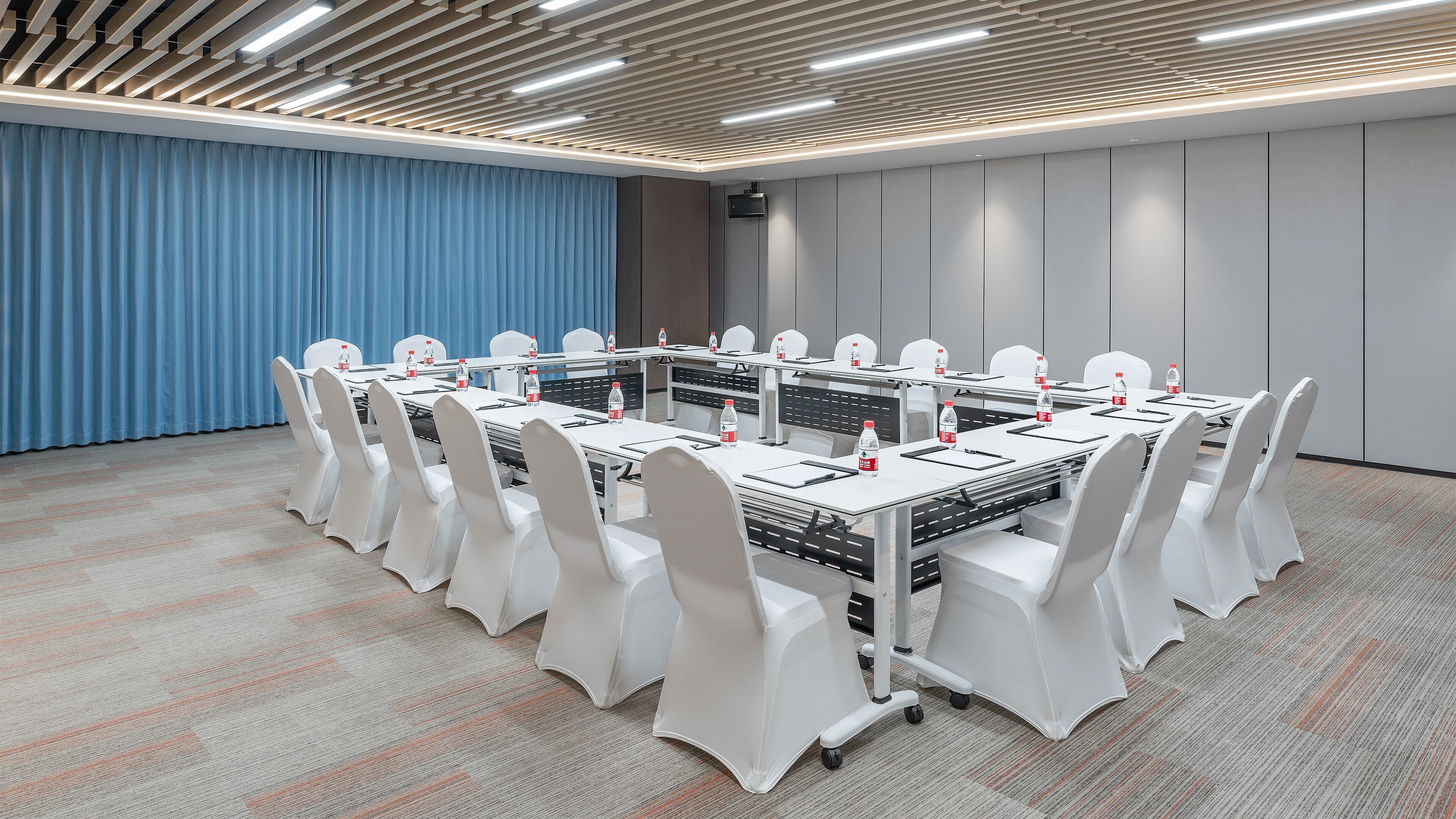 Un salón de conferencias con una larga mesa, sillas blancas y un telón azul de fondo.