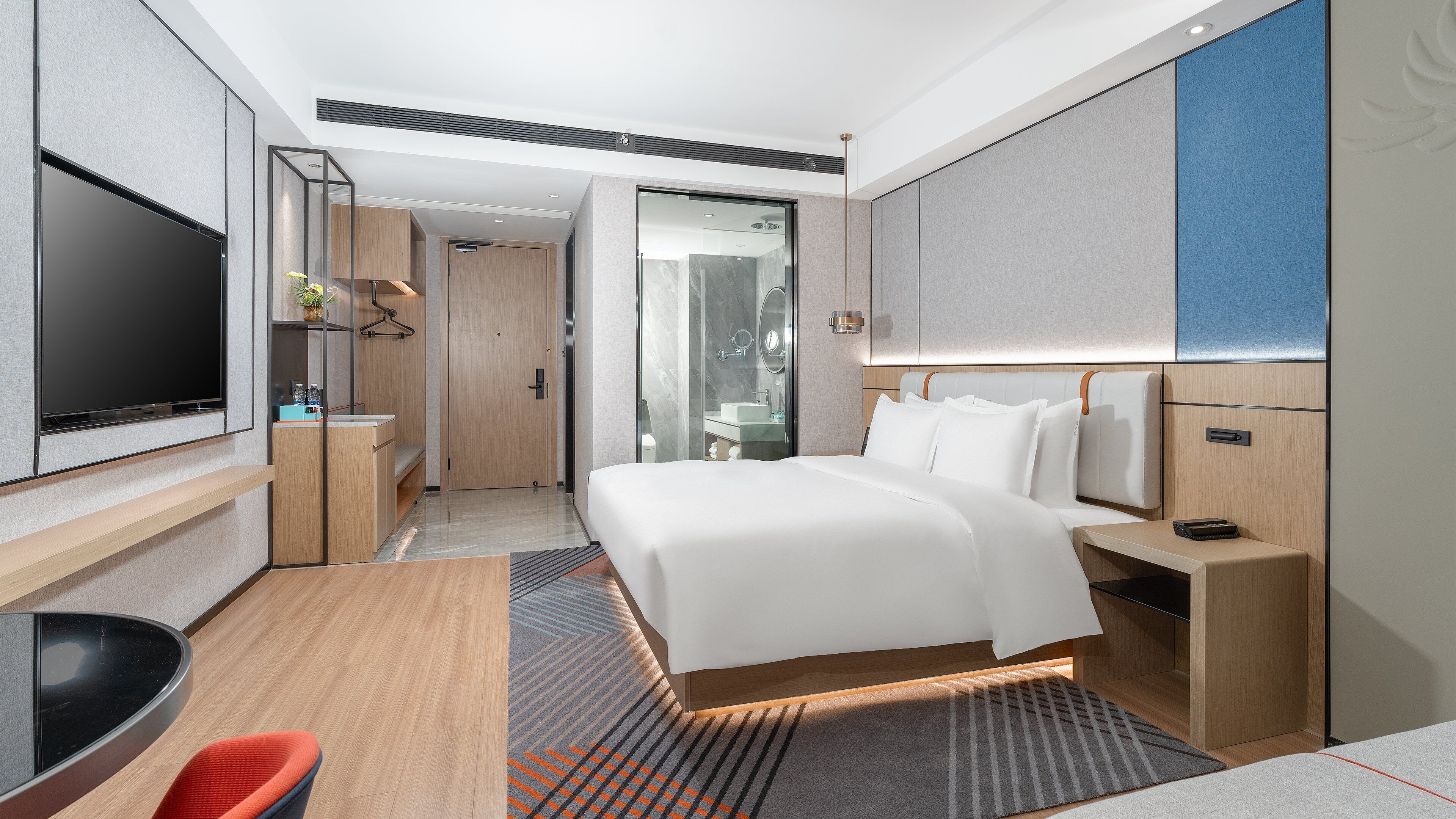 Een moderne hotelkamer met een groot bed, een bureau, een flatscreen televisie en een badkamer zichtbaar achter een glazen deur.