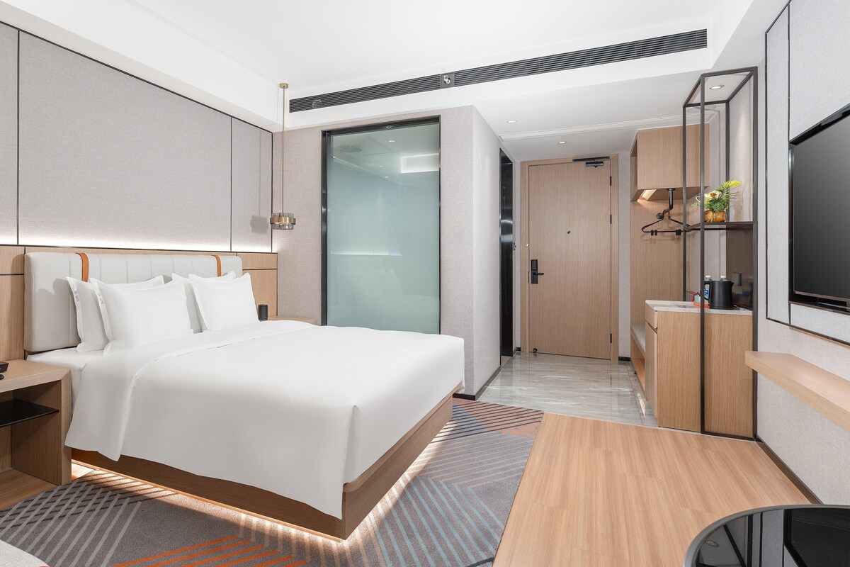 A modern hotel room with a large bed, bedside tables, a desk, a flat-screen TV, and a sliding door closet.
