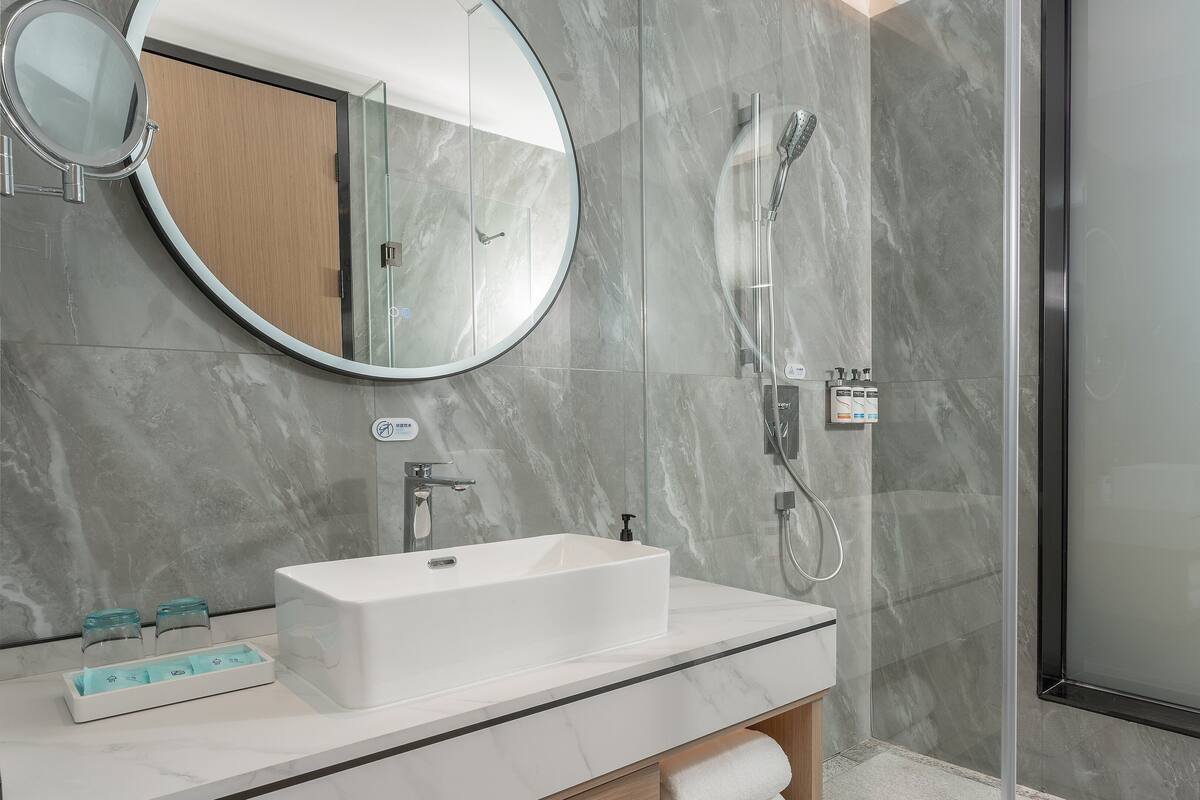 A modern bathroom with a rectangular sink, a round mirror, and a glass-enclosed shower.