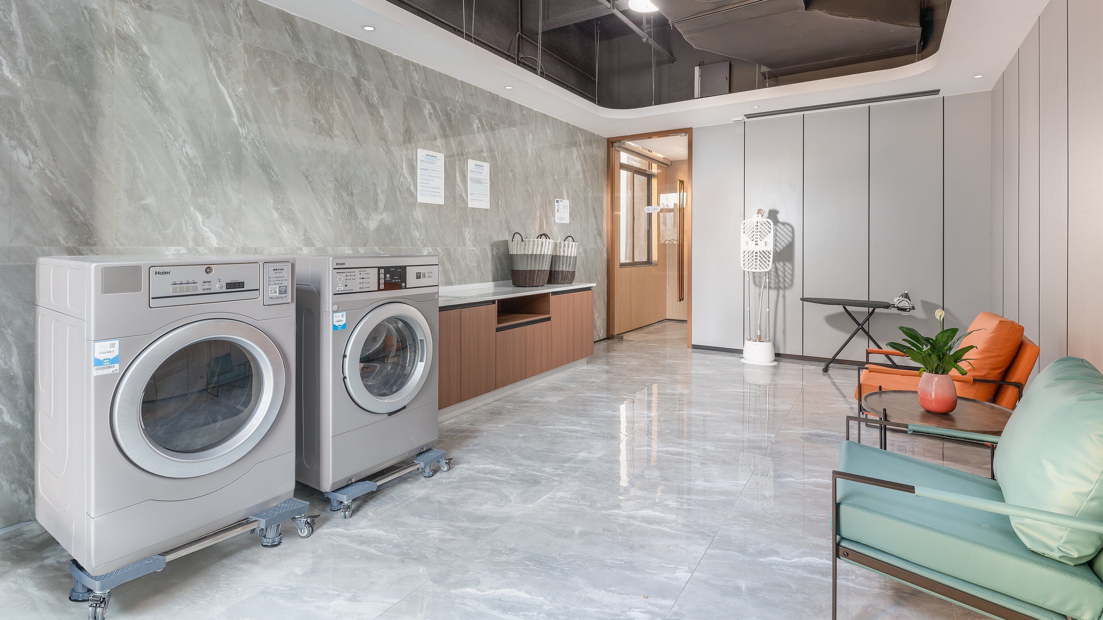 A modern laundry room with two Haier washing machines, a wooden counter, and a seating area with a table and chairs.