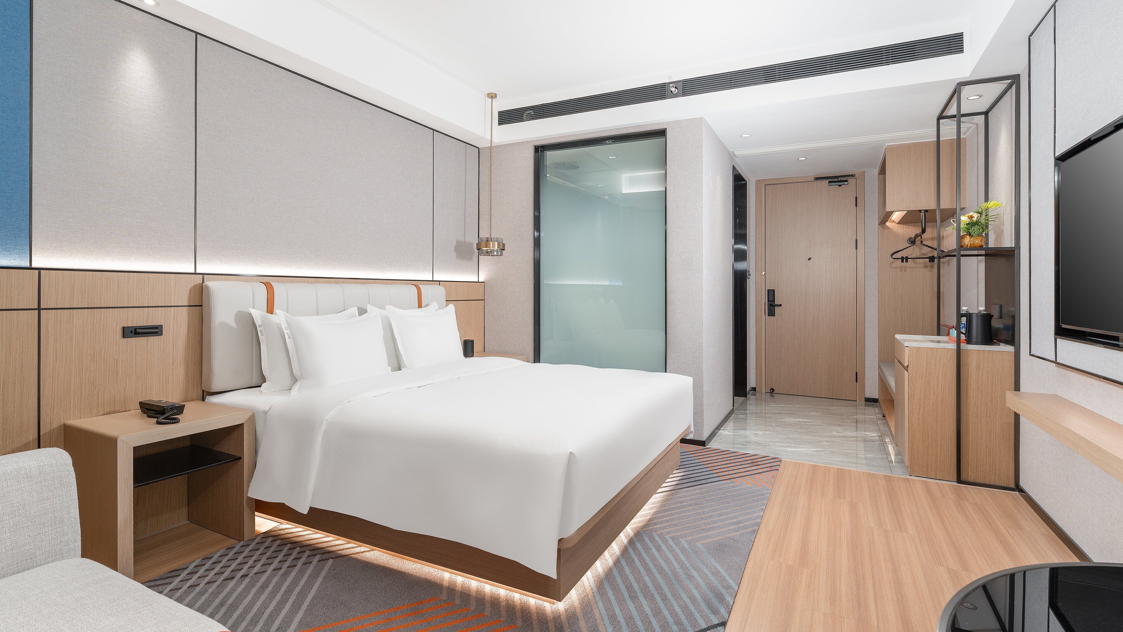A modern hotel room with a large bed, bedside tables, a desk, a flat-screen TV, and a sliding door closet.