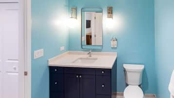 A bathroom with a white sink, dark blue cabinets, a white toilet, and a mirror with wall-mounted lights.