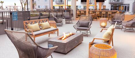 An outdoor seating area with wicker chairs, a fire pit, and a bar with umbrellas.