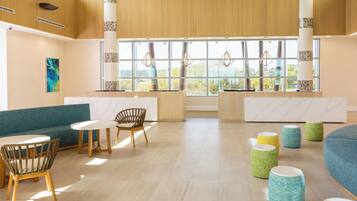 A modern lobby with a blue sofa, wooden chairs, a marble reception desk, and a large window with a view of greenery.
