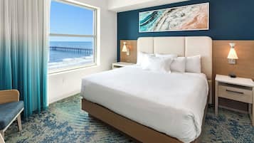 A hotel room with a large bed, a view of the ocean, a wooden headboard, and a painting on the wall.