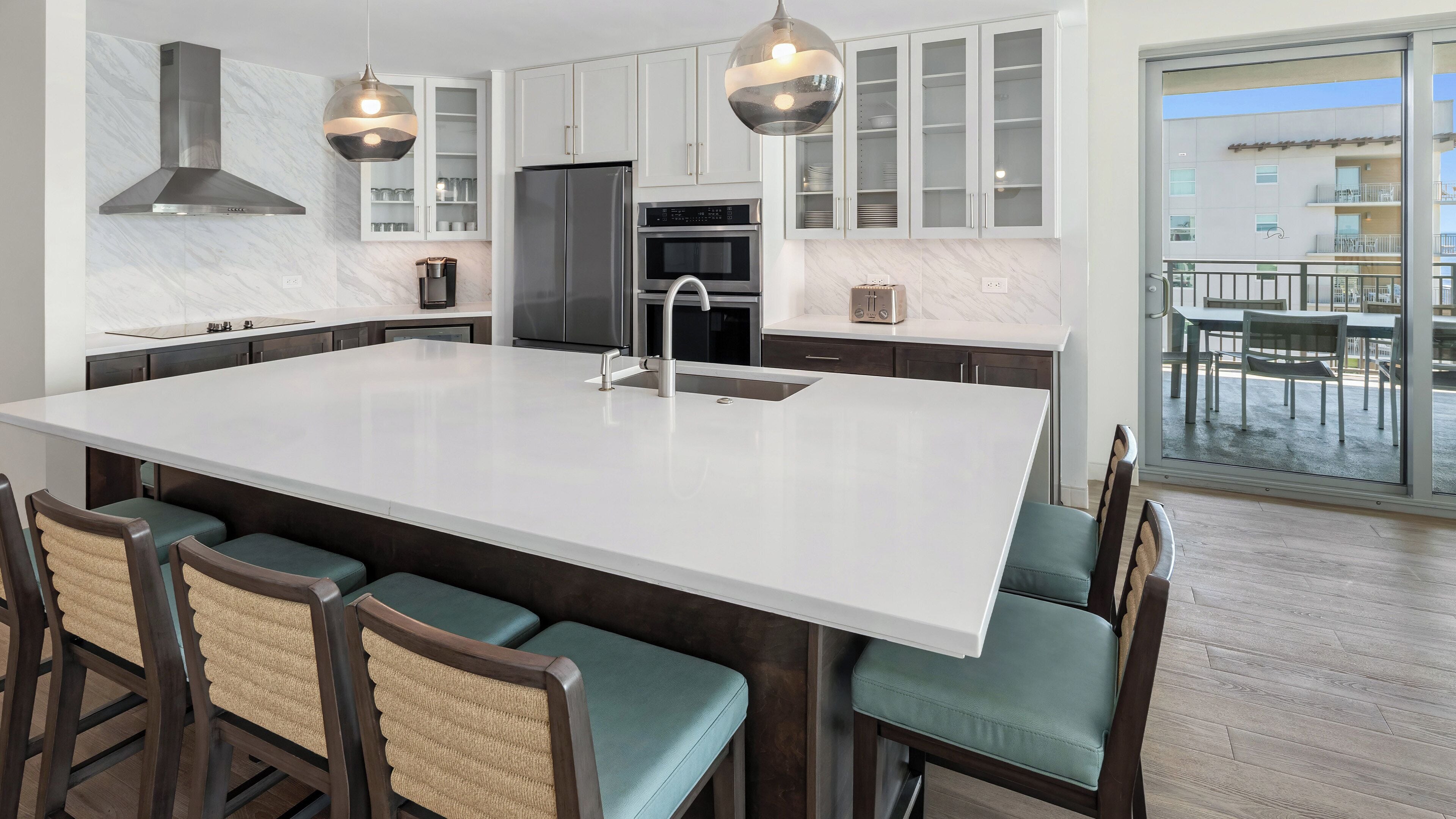 A modern kitchen with a large island, stainless steel appliances, and a view to the outside.