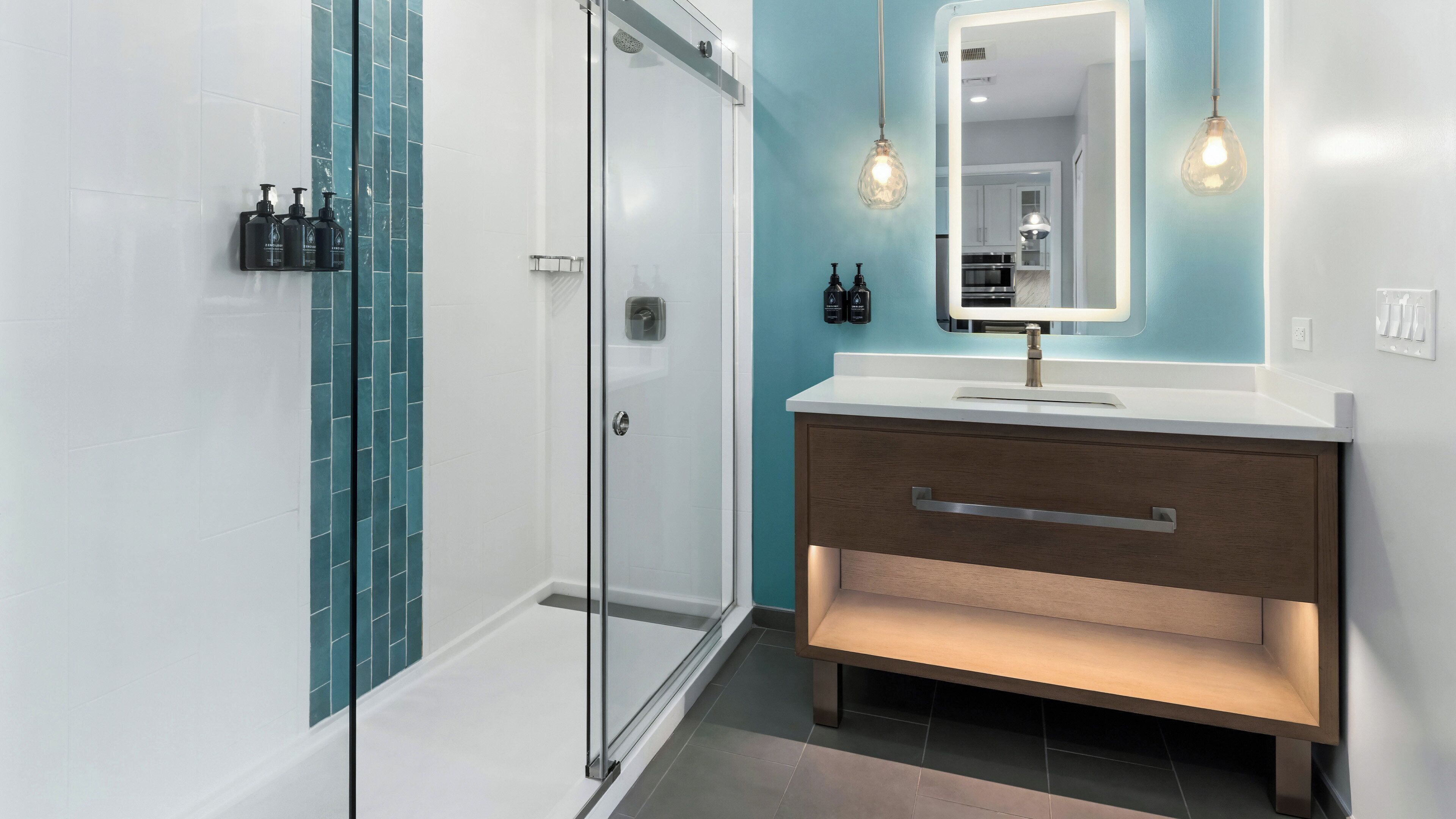 Une salle de bain moderne avec une douche à parois de verre, un meuble-lavabo avec miroir et des luminaires suspendus.