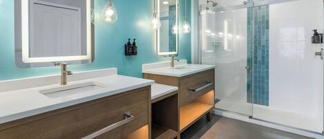 A modern bathroom with two sinks, wooden cabinets, and a glass shower enclosure.