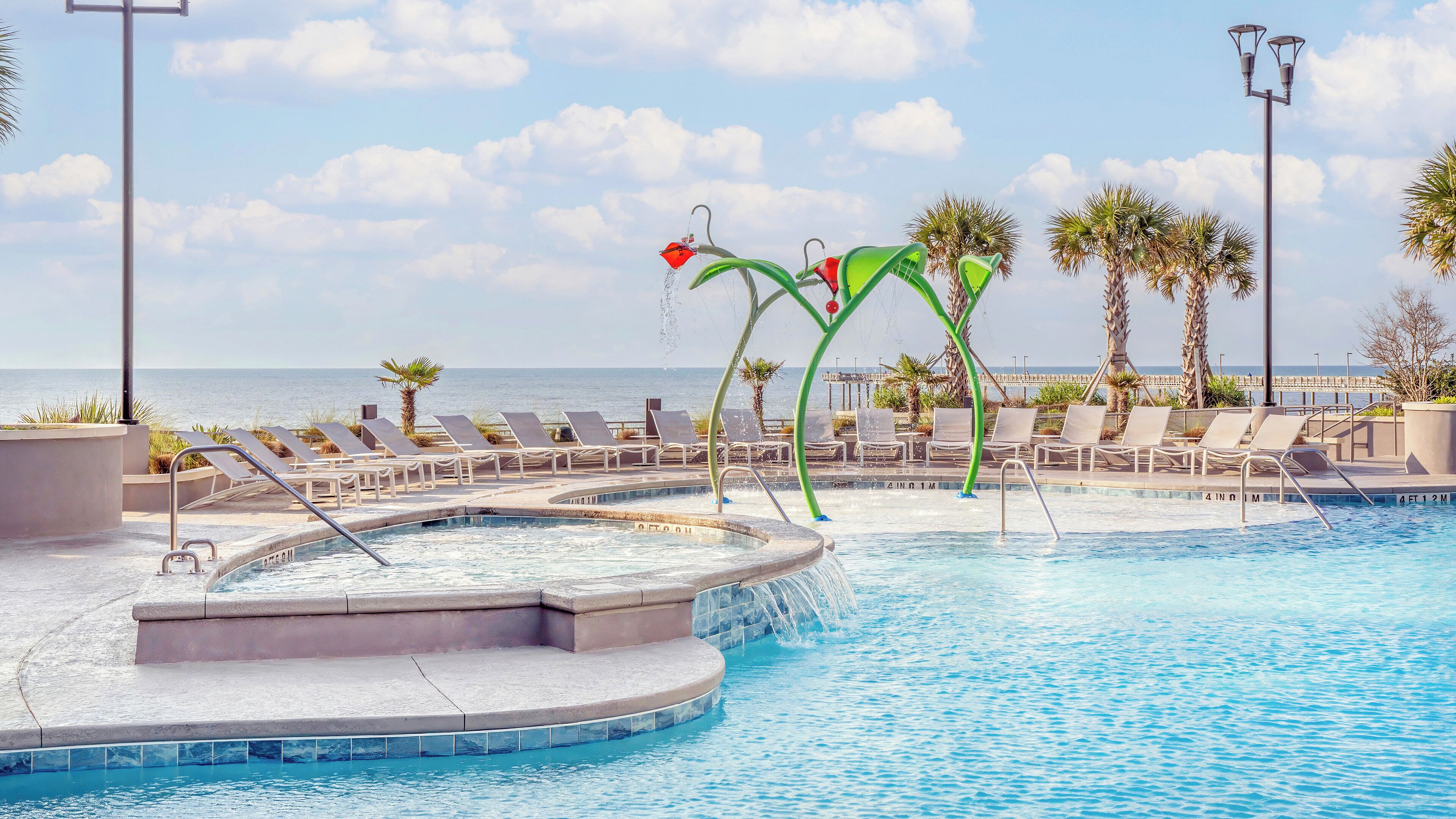 A pool area with lounge chairs and a view of the sea.