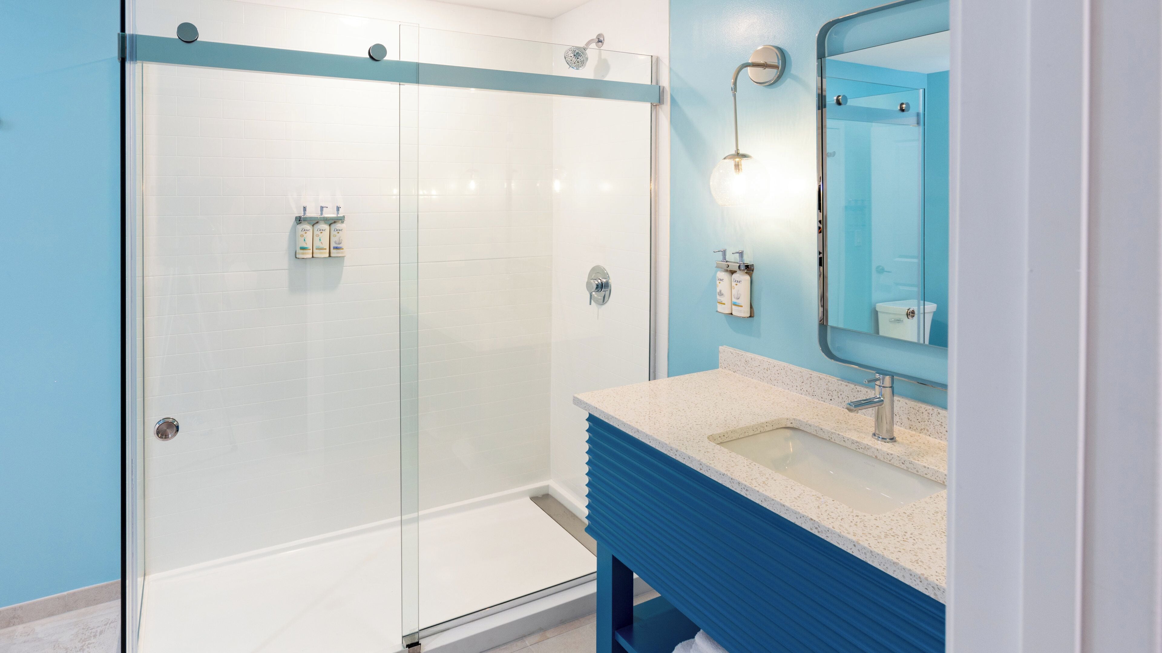 Un baño moderno con ducha envuelta en vidrio, un lavamanos con tocador azul y un espejo.