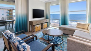 A hotel room with a large window, a flat-screen TV, a sofa, a chair, a small table, and a balcony with a view of the beach. - Holiday Inn Club Vacations Myrtle Beach Oceanfront by IHG (Myrtle Beach)