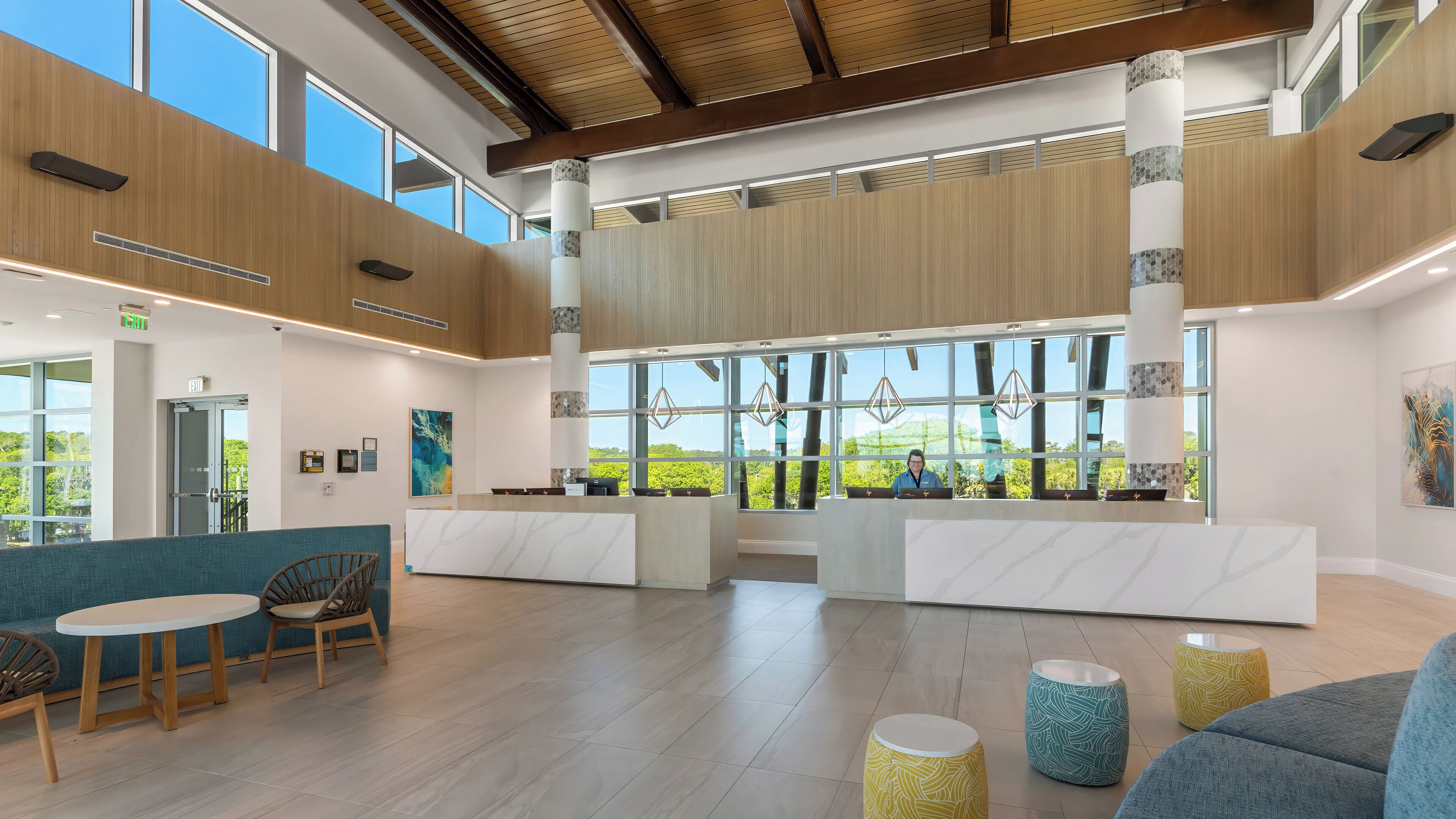 A spacious lobby with a reception desk, seating area, and large windows offering a view of greenery.