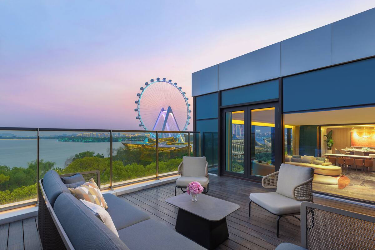 A modern outdoor balcony with a view of a Ferris wheel, seating, and a dining area.