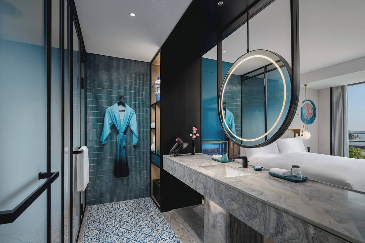 A modern hotel bathroom with a large mirror, a marble sink, and a shower area.