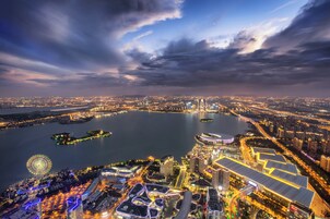 Vista panorâmica de um horizonte urbano noturno, com edifícios iluminados, uma grande massa de água e uma roda-gigante.