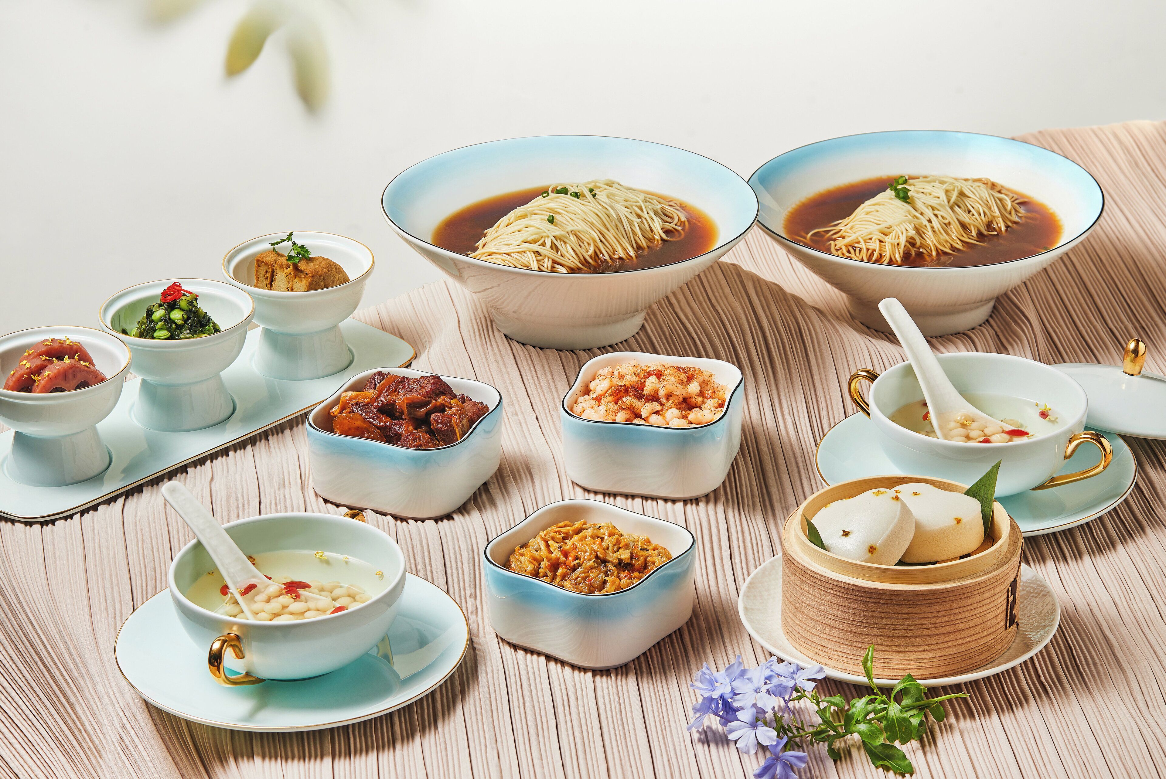 Une variété de plats asiatiques, notamment des nouilles et de petits bols contenant différentes sauces, disposés sur une table.