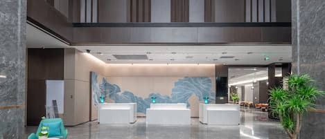 Un hall d’entrée moderne avec un sol en marbre, un comptoir d’accueil, un espace salon et un grand mur décoratif.
