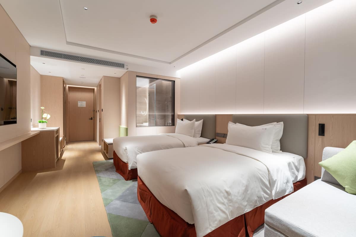 Ein modernes Hotelzimmer mit zwei Betten, einer kleinen Küchenzeile, einem Badezimmer und einem großen Fenster.