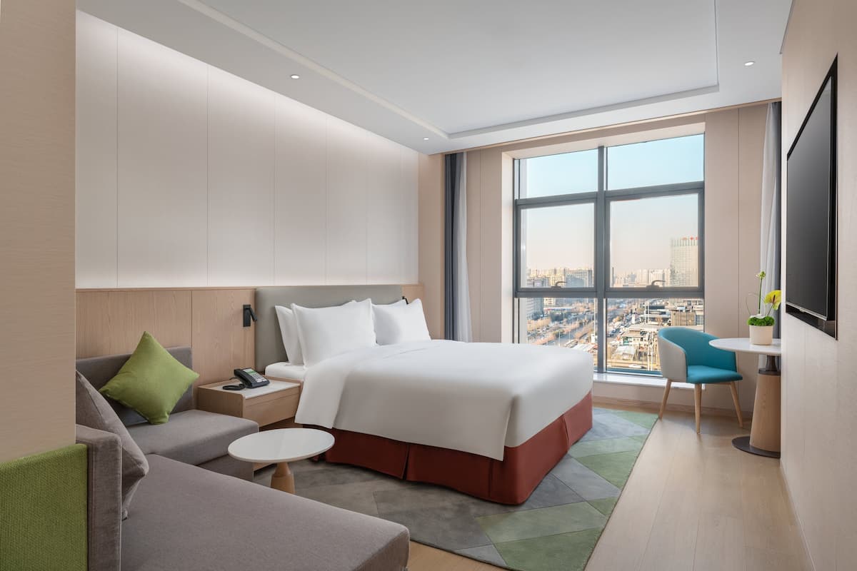 Ein modernes Hotelzimmer mit einem großen Bett, einer Couch, einem kleinen Tisch und einem Fernseher.