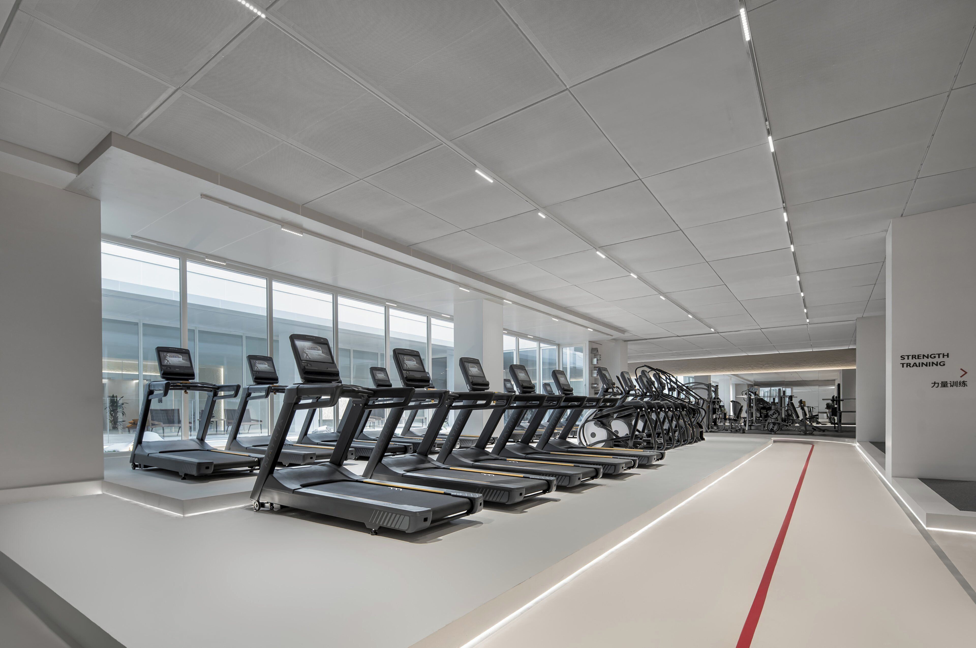 Un gimnasio moderno con cintas de correr alineadas a lo largo de una pista central, ventanas amplias y un diseño limpio y minimalista.