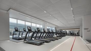 Un gimnasio moderno con cintas de correr alineadas a lo largo de una pista central, ventanas amplias y un diseño limpio y minimalista.