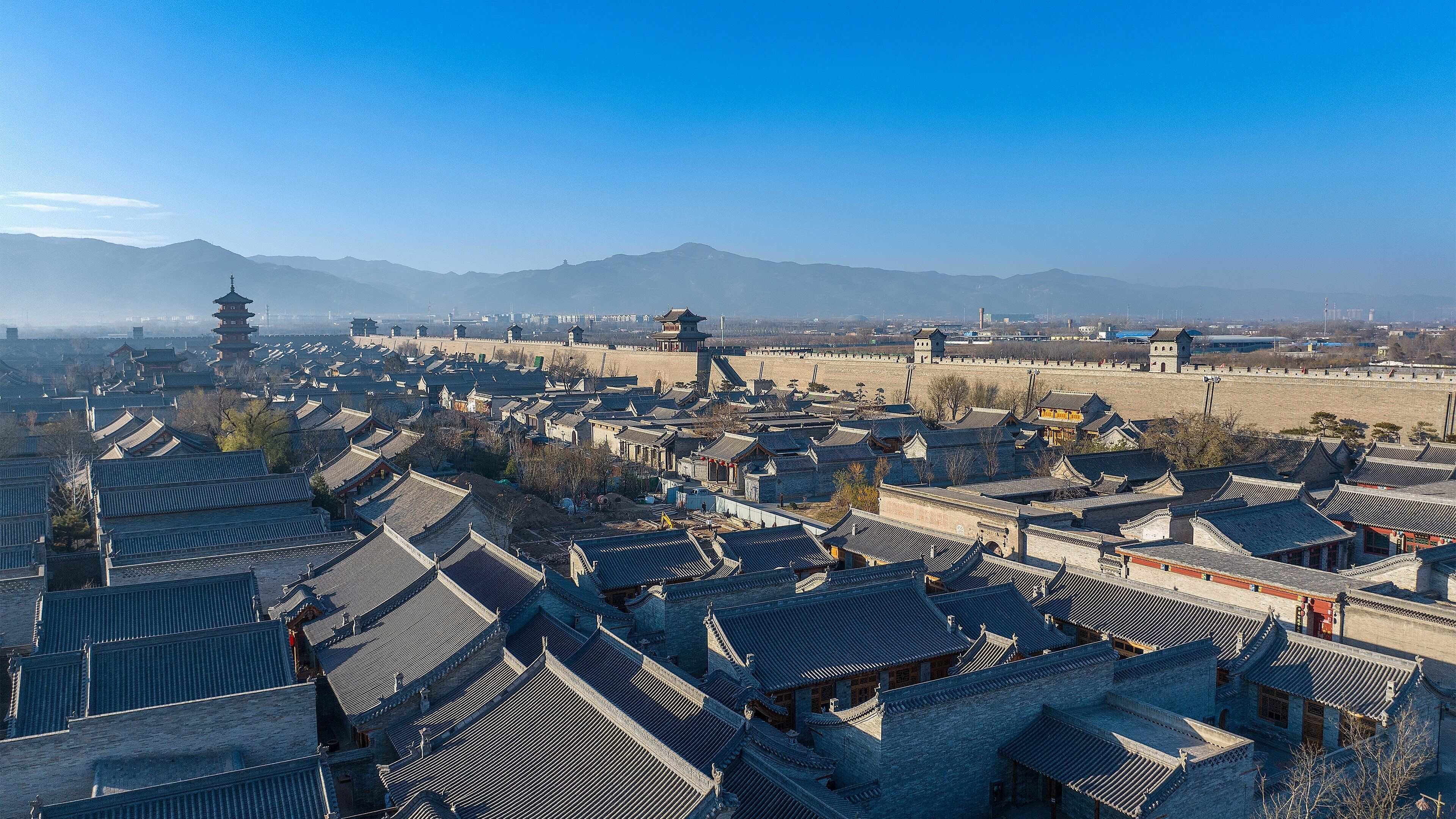 A traditional Chinese town with pagoda-style buildings and a large wall in the background.