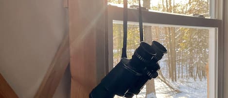 Un télescope suspendu près d’une fenêtre, avec une vue sur un paysage enneigé.