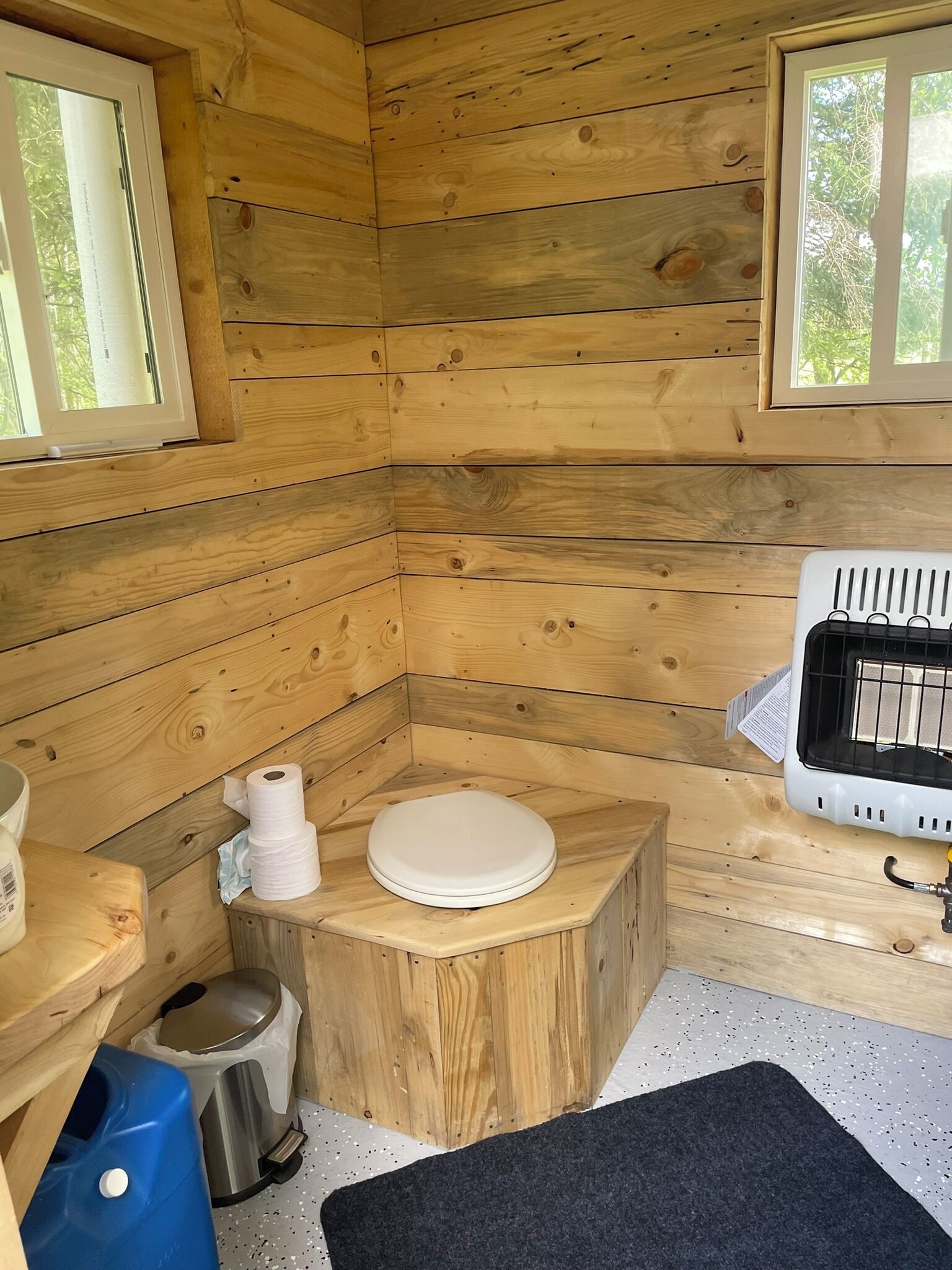 Eine kleine Holzhütte mit Toilette, einem kleinen Waschbecken und einer Heizung.