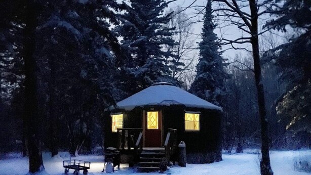 Une cabane dotée d’une terrasse en bois, d’un porche abrité et surplombant un paysage enneigé.