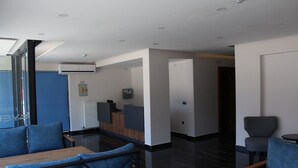 Un área de recepción moderna con un mostrador, zona de estar con sillas tapizadas en azul y suelo de baldosas negras.