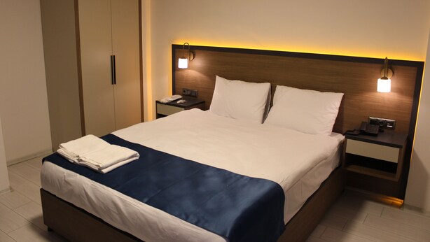 Habitación de hotel con una cama grande, un armario, mesitas de noche con lámparas y una mesita auxiliar.