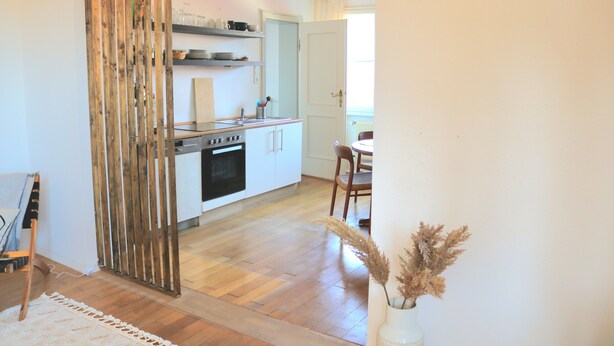 A modern kitchen with wooden flooring, white cabinets, and a dining area with a table and chairs. - Wohnung am Bergpark Wilhelmshöhe (Kassel)