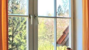 A window with a view of trees and a building. There are three small containers on the windowsill. - Wohnung am Bergpark Wilhelmshöhe (Kassel)