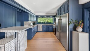 Una cocina moderna con armarios azules, un refrigerador de acero inoxidable y un amplio ventanal con vista a zonas verdes.