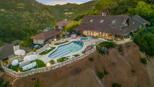 Una casa grande con piscina, rodeada de colinas y árboles.